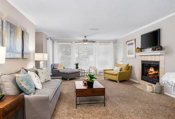 Light-filled carpeted living room that has a tile-surround fireplace, floor-to-ceiling windows and a ceiling fan.